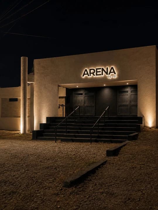 El frente de ARENA de noche: el cartel iluminado sobre la puerta, la escalera de entrada y la grava